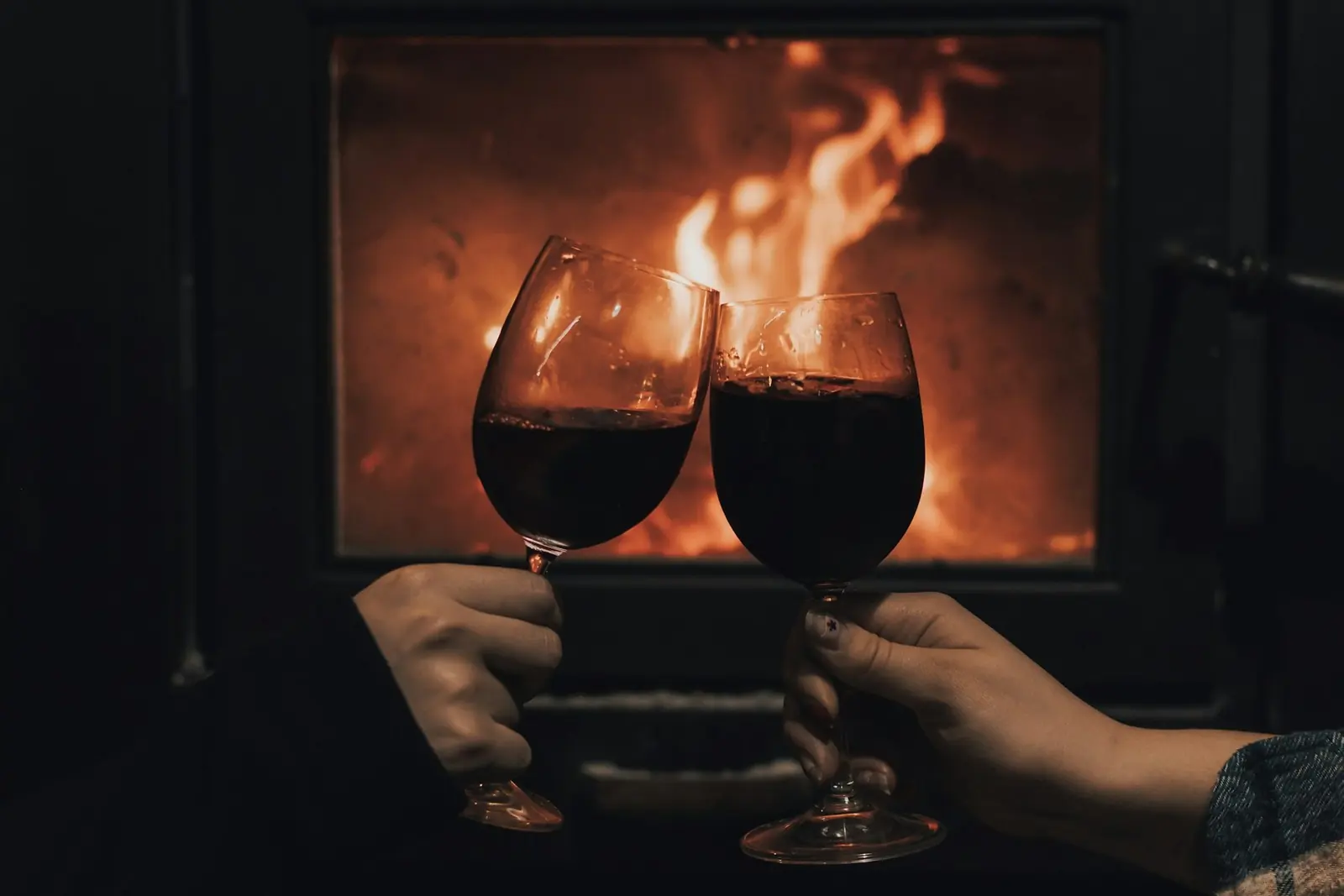 Dois copos de vinho a brindar diante da lareira, uma noite aconchegante a dois.